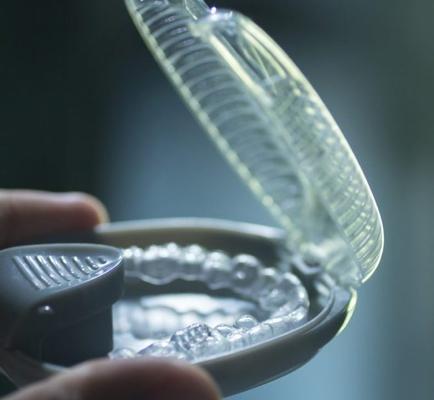 A close up shot of a hand holding Invisalign braces from the Den